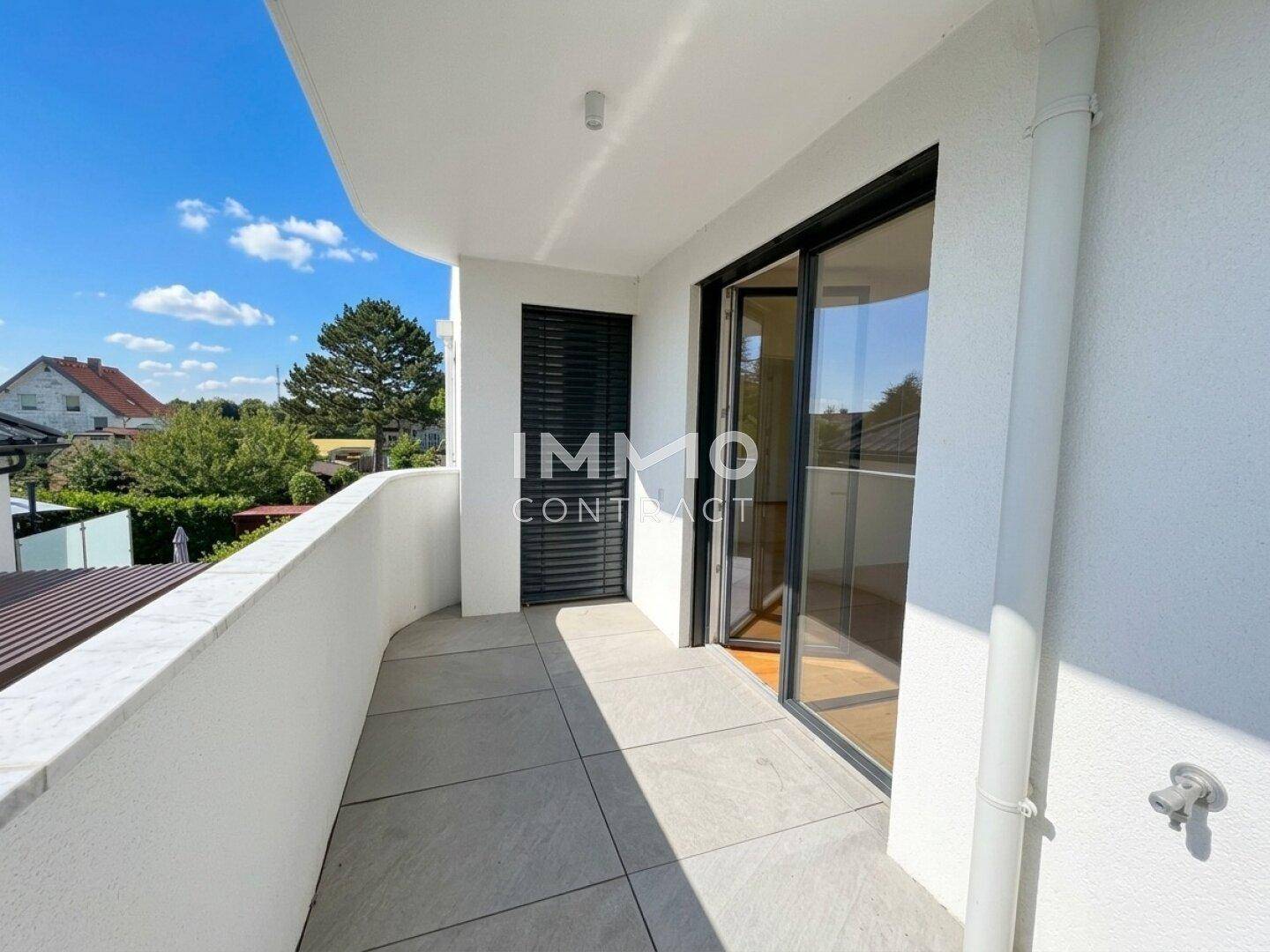 Moderner Balkon mit Fliesenboden und Blick auf die Umgebung, mit geschlossenen Rollläden.