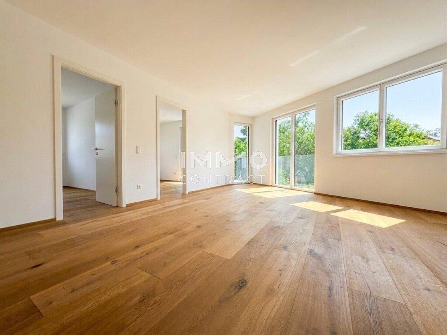 Heller Wohnraum mit hochwertigem Holzparkettboden, großen Fenstern und Zugang zum Außenbereich.
