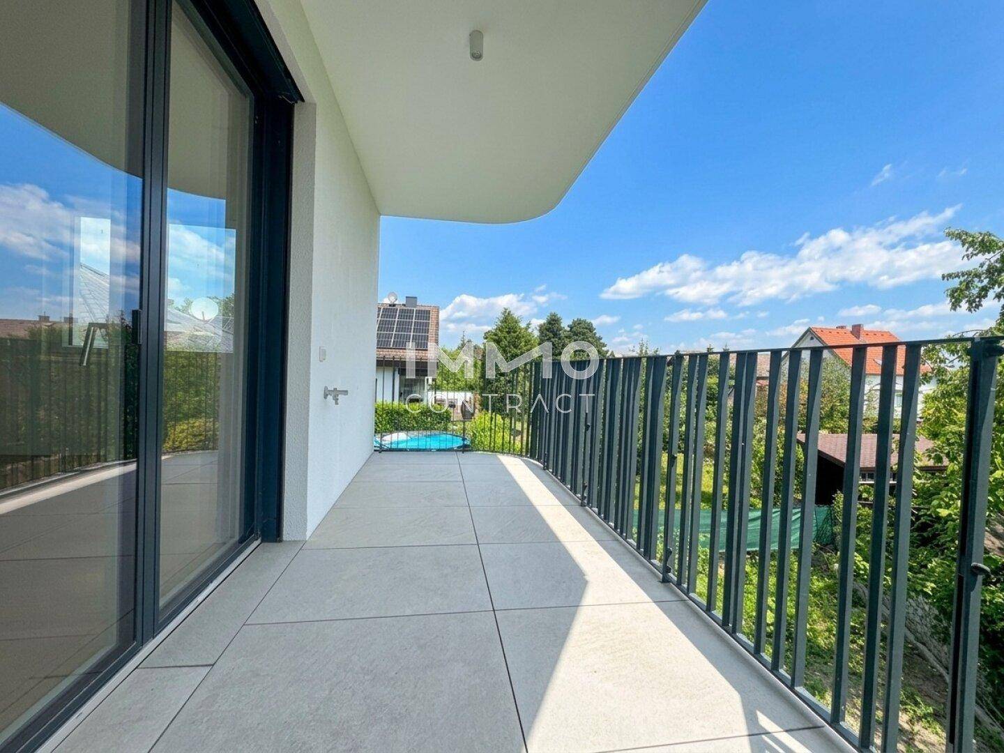 Breiter Balkon mit Fliesenboden und schwarzem Metallgeländer, bietet einen weiten Blick ins Grüne.
