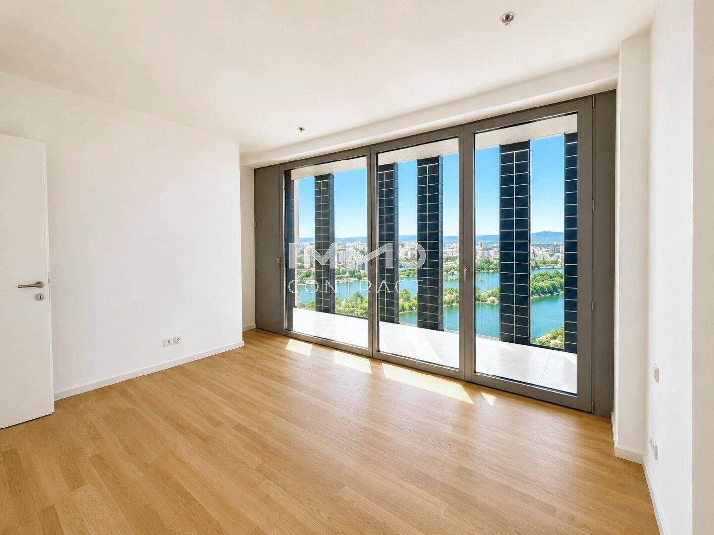 Geräumiges Zimmer mit Holzboden und großen Fenstern, die einen beeindruckenden Blick auf die Stadt und das Wasser bieten.