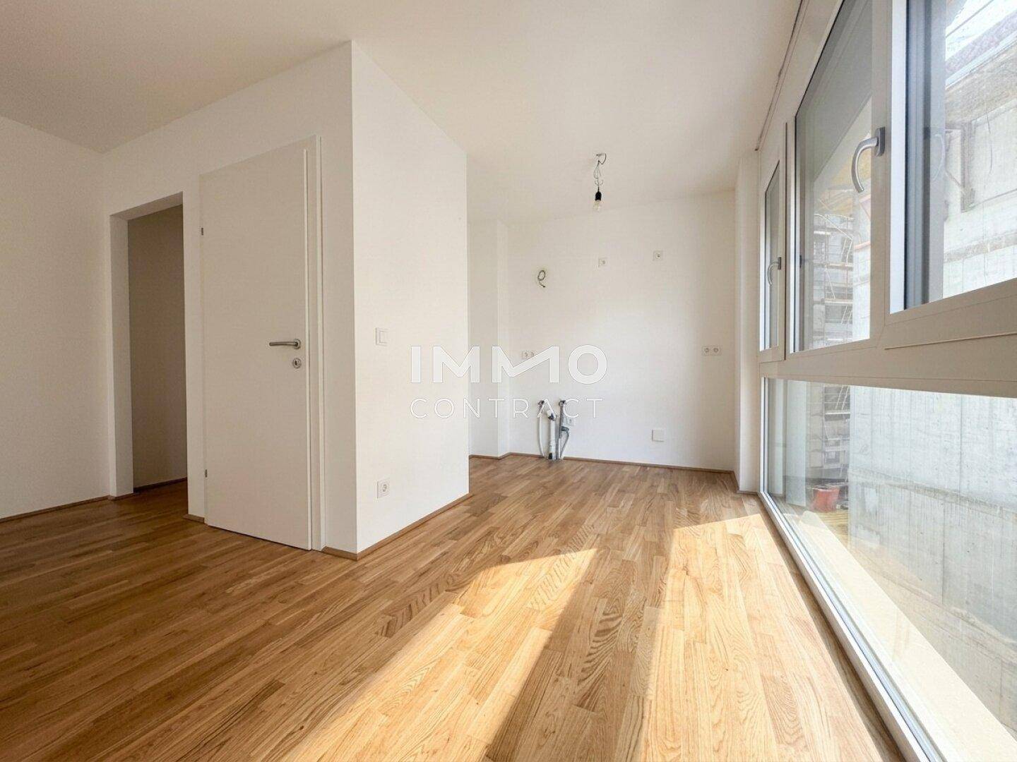 Leerer Küchenbereich mit Anschlüssen, Parkettboden und viel Tageslicht durch große Fenster.