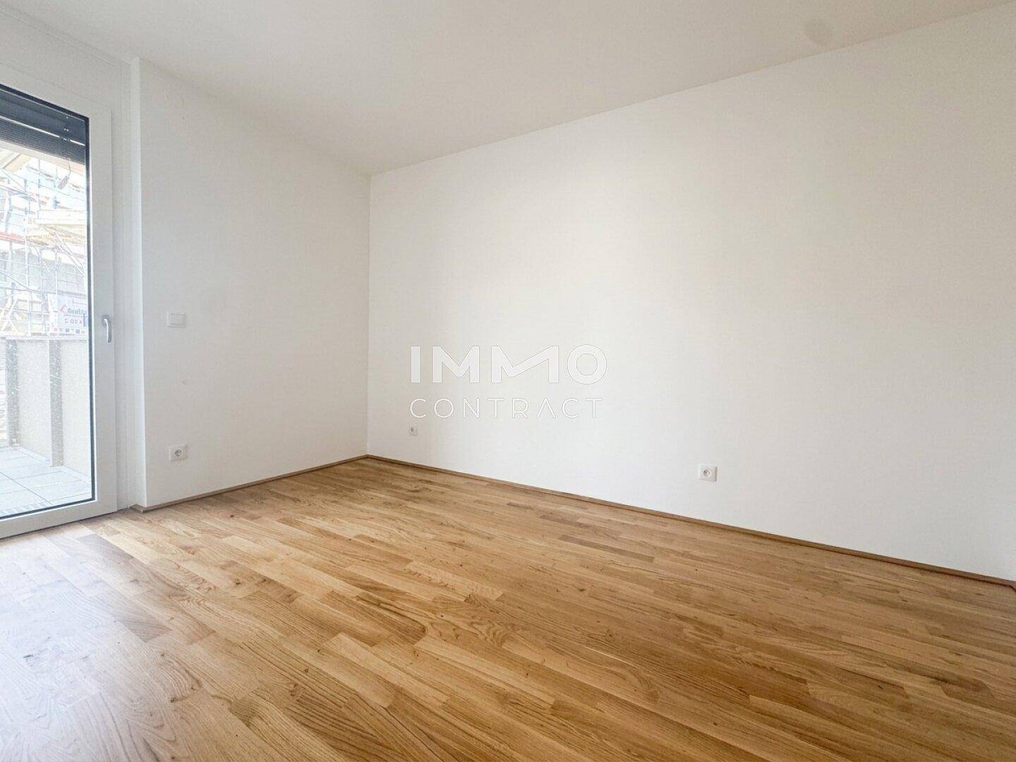 Heller Raum mit Parkettboden und Zugang zu einem Balkon, ideal als Schlafzimmer.