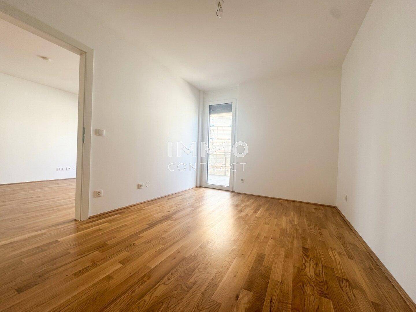 Helles Zimmer mit Parkettboden und Zugang zu einem Balkon oder einer Terrasse, ideal als Schlafzimmer.