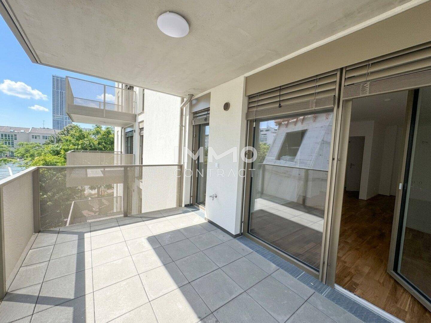 Heller Balkon mit Fliesenboden und Glasgeländer, bietet einen Blick auf die Umgebung.