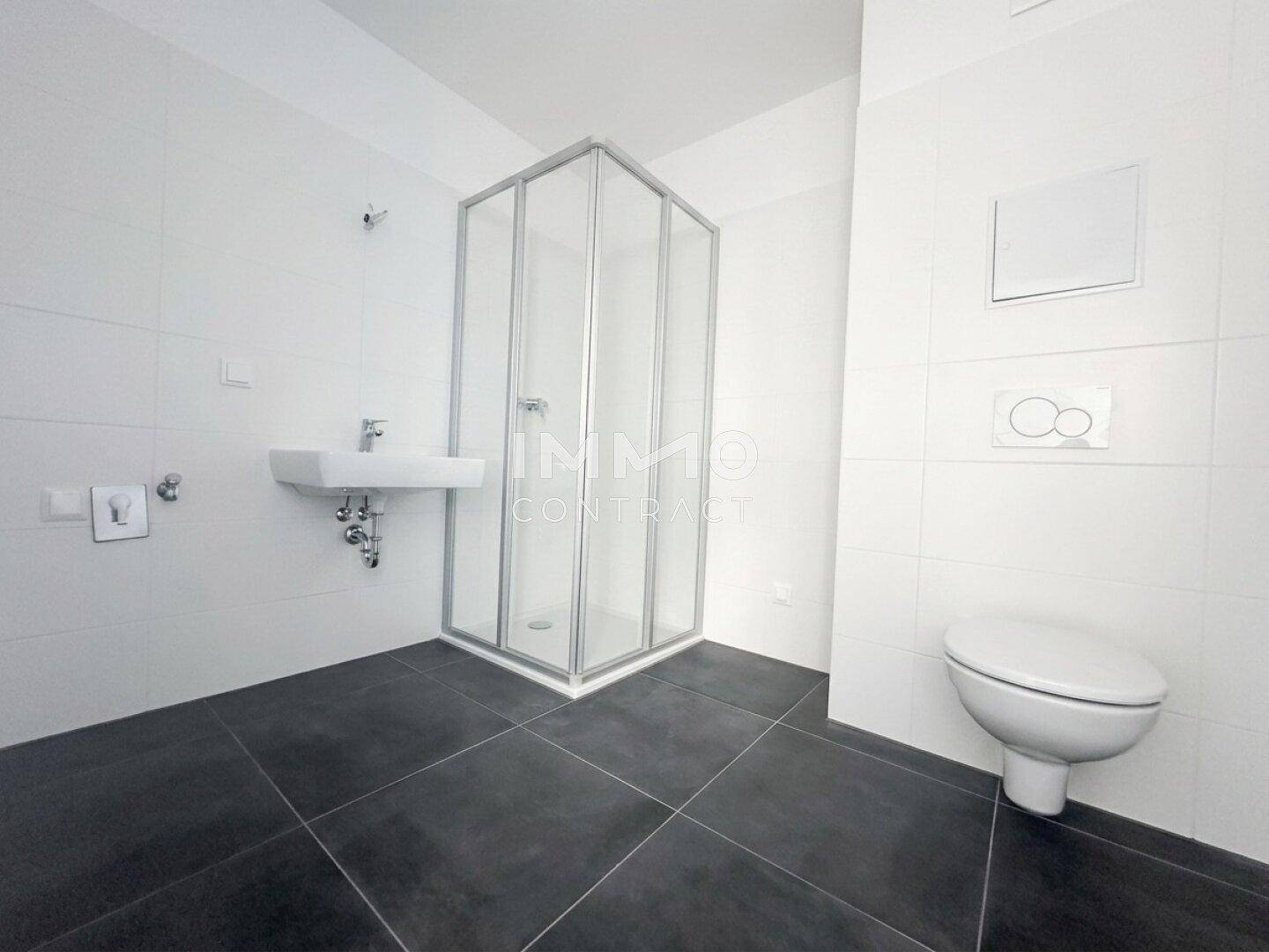Modernes Badezimmer mit dunklen Bodenfliesen, weißer Wandverkleidung und Duschkabine.
