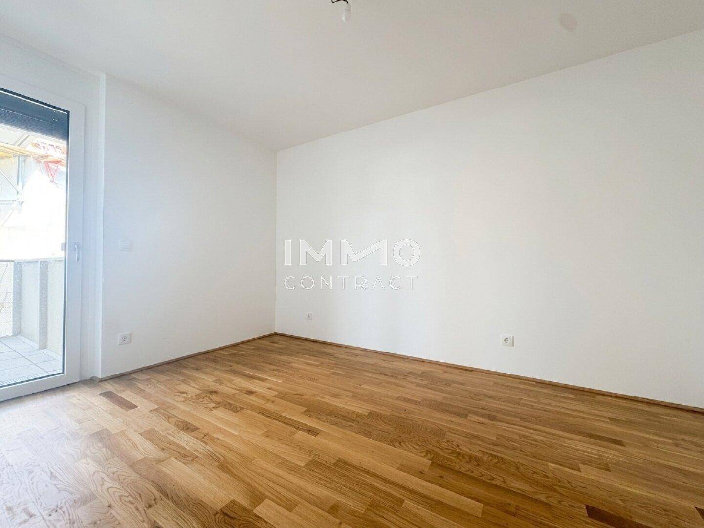 Helles, leeres Zimmer mit Holzboden und Zugang zu einem kleinen Außenbereich.