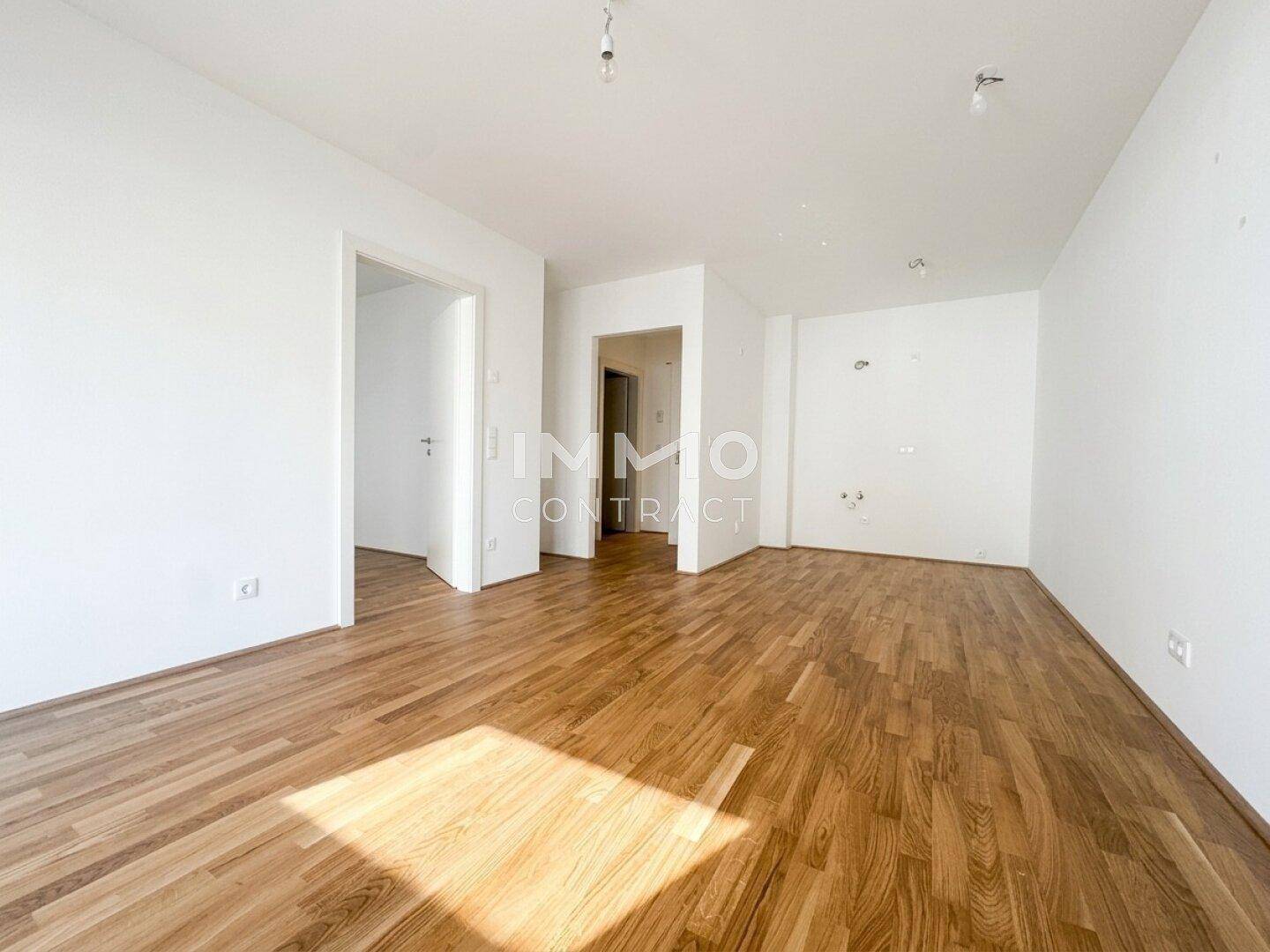 Geräumiges, leeres Wohnzimmer mit Holzboden und mehreren Türöffnungen zu anderen Räumen.