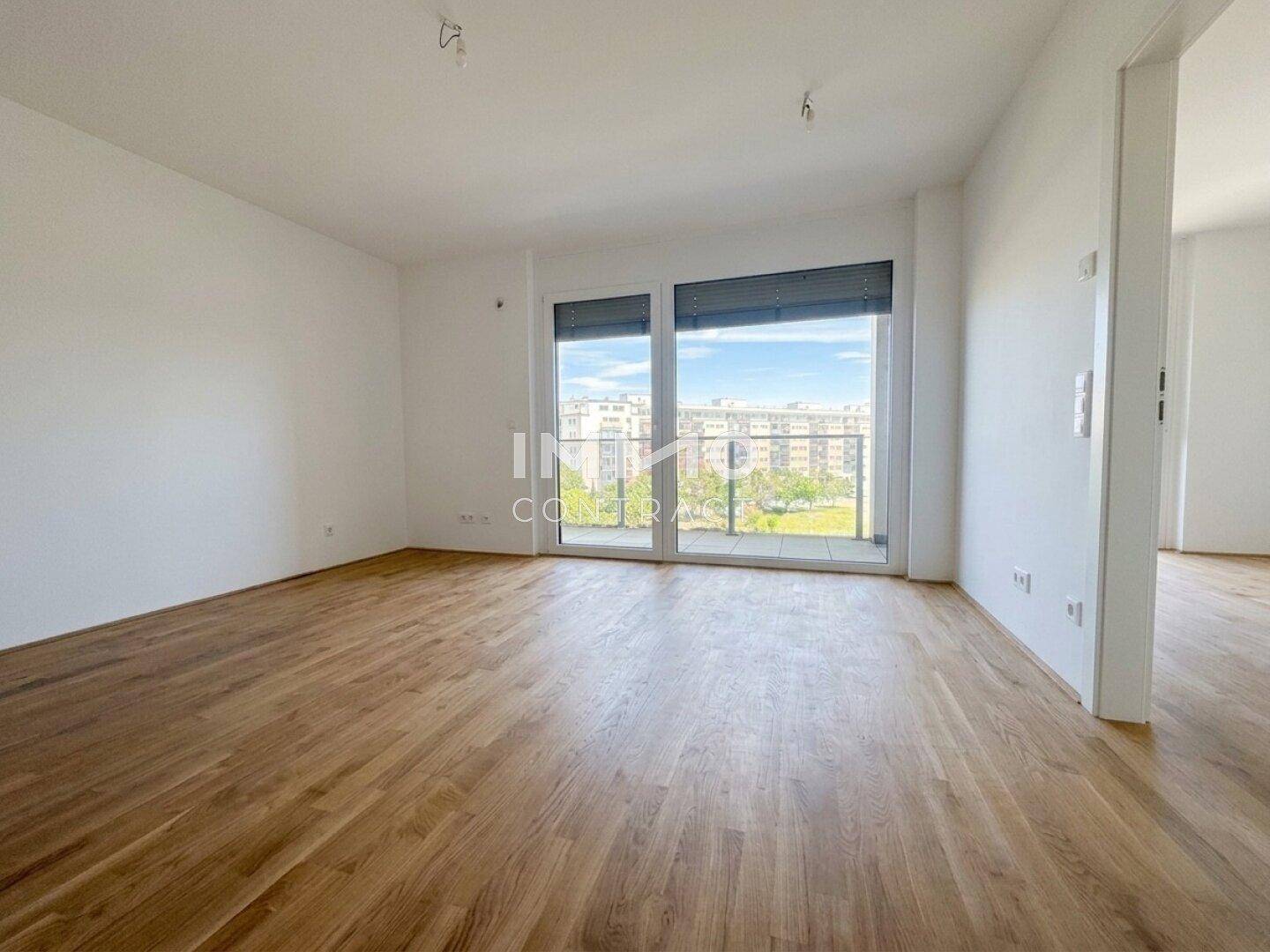 Geräumiger, heller Raum mit Holzparkett und großen Fenstern, die viel Tageslicht hereinlassen.