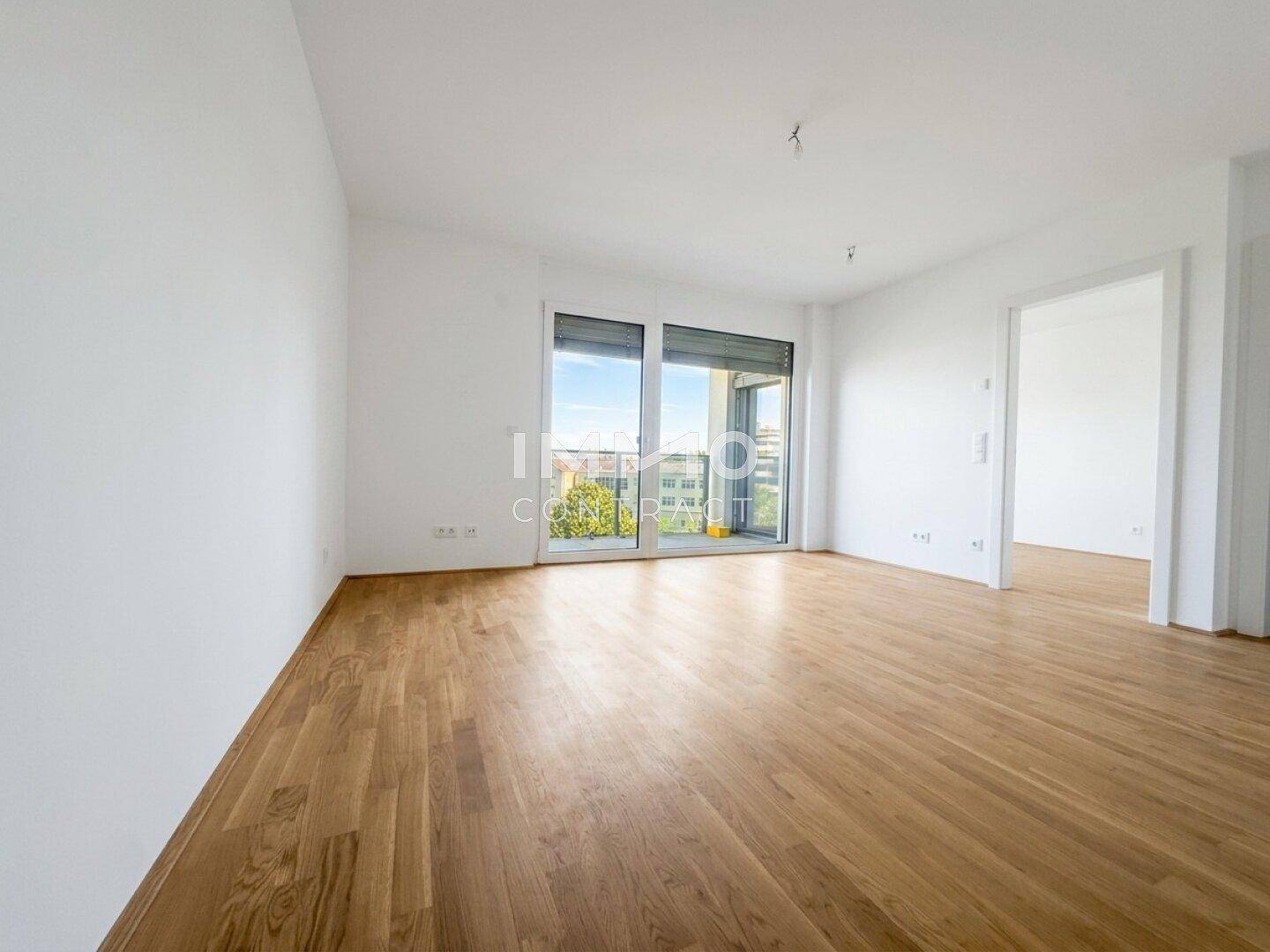 Heller, leerer Raum mit Parkettboden und Zugang zu einem Balkon oder einer Terrasse.
