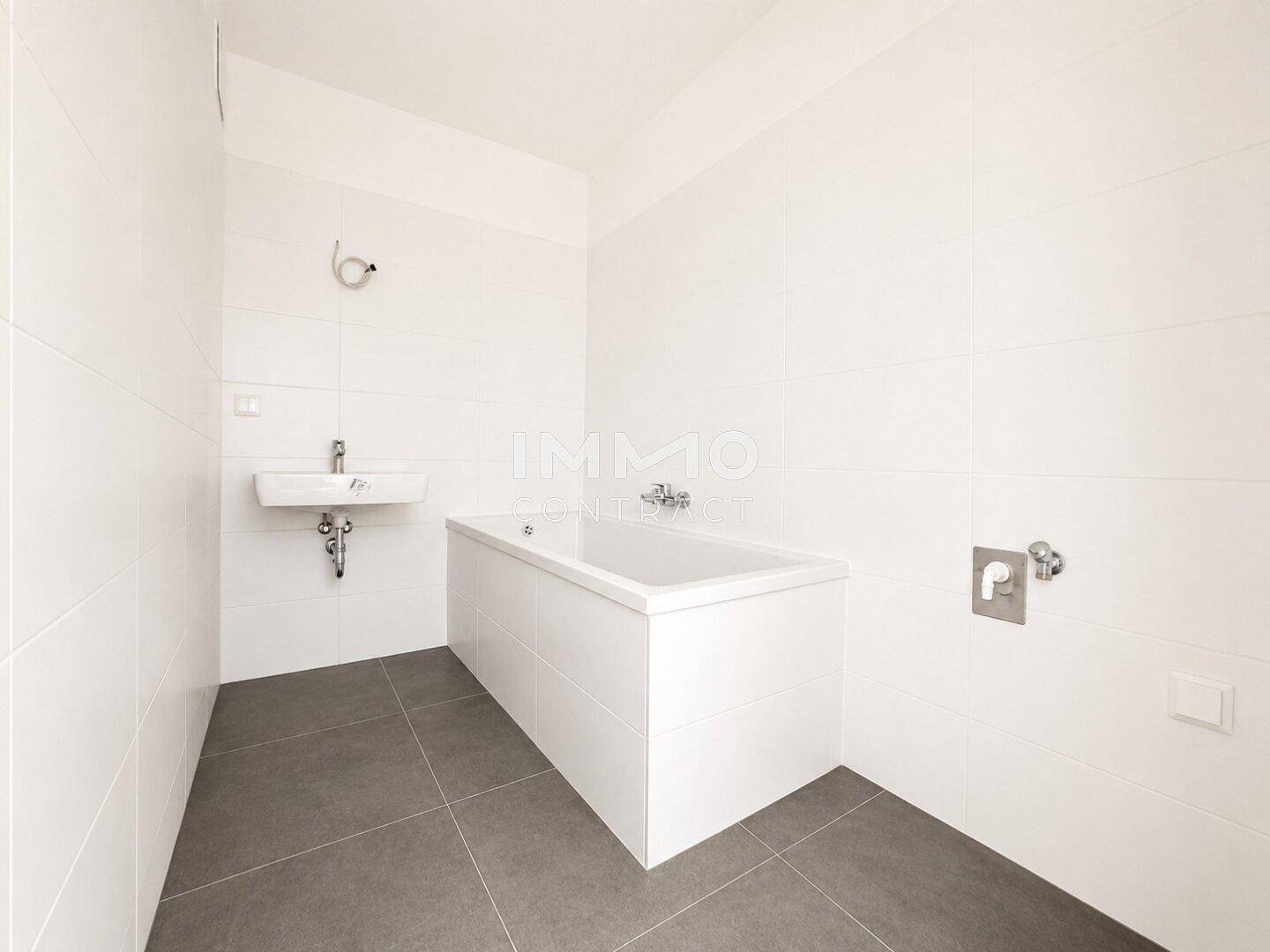 Modernes Badezimmer mit weißer Badewanne, Wandfliesen und grauem Fliesenboden.