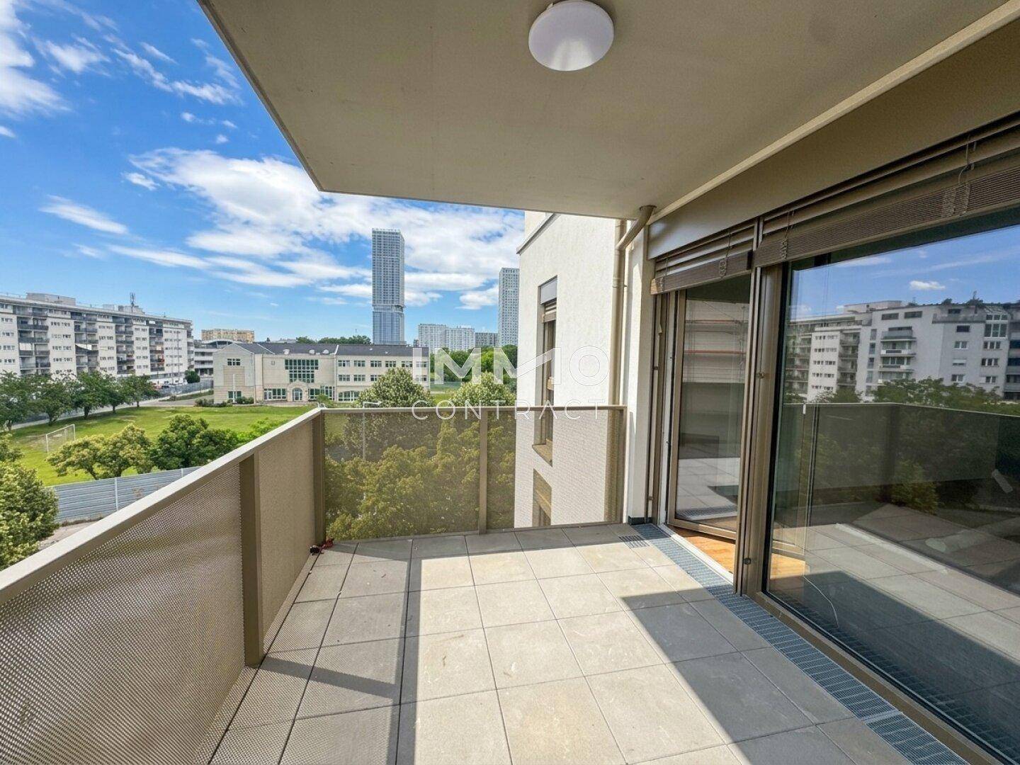 Geräumiger Balkon mit Fliesenboden und Blick auf die Stadt und Grünflächen.