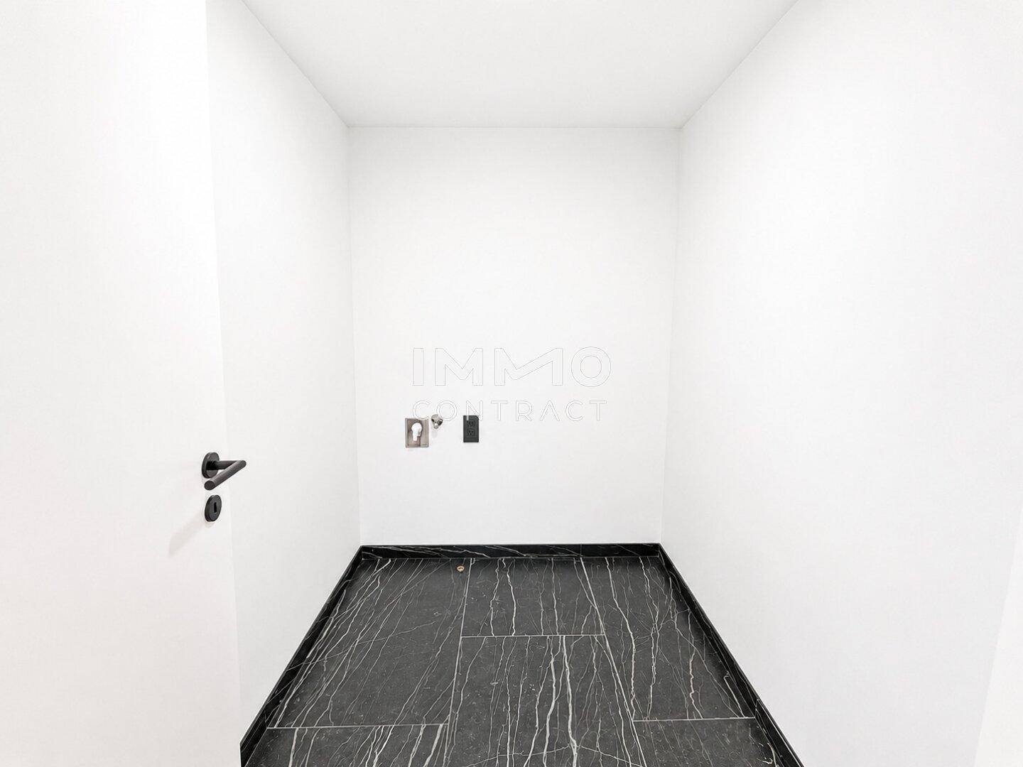 Kleiner, leerer Hauswirtschaftsraum mit dunklem Fliesenboden und Anschlüssen für Waschmaschine.