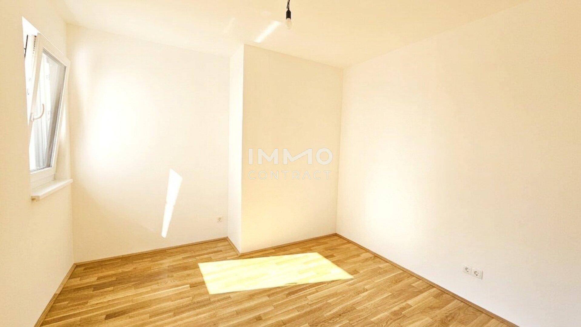 Leeres, helles Zimmer mit Parkettboden und einem Fenster, das viel Tageslicht hereinlässt.