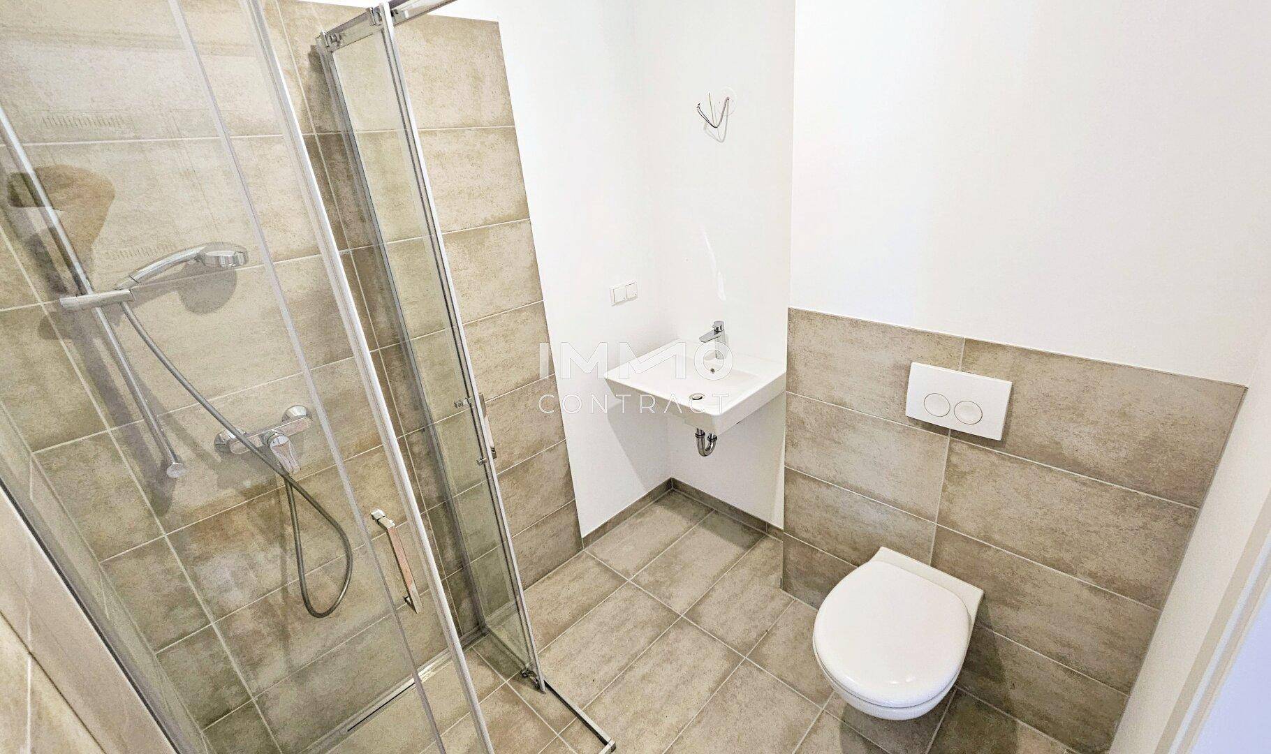 Modernes Badezimmer mit Duschkabine, WC und Waschbecken, ausgestattet mit hellen Fliesen.