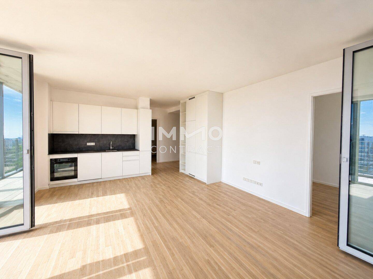 Offener Wohnbereich mit integrierter Küche, Holzboden und viel Tageslicht durch große Fenster.