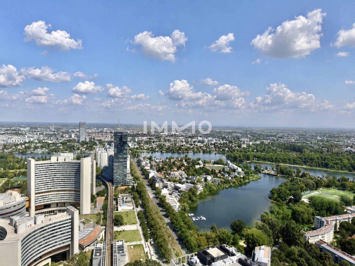 Weitläufiger Blick über die Stadtlandschaft mit Fluss, Gebäuden und Grünflächen unter blauem Himmel.