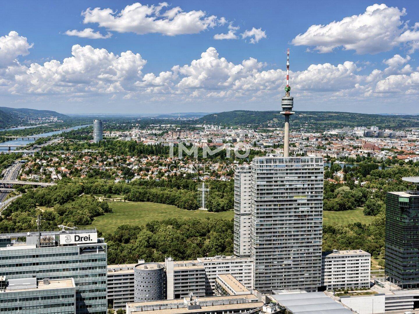Luftaufnahme der Stadt mit dem Donauturm, Hochhäusern und ausgedehnten Parkanlagen.
