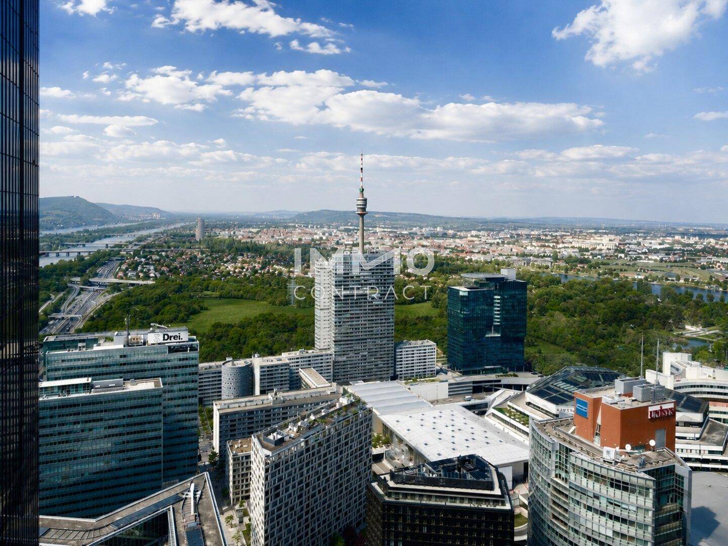 Weitläufige Luftaufnahme des modernen Stadtzentrums mit Hochhäusern und dem Donauturm in der Ferne.
