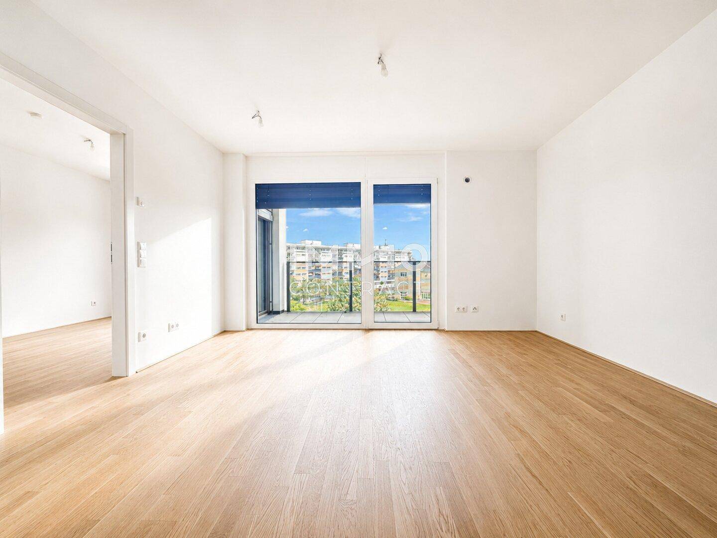Geräumiges, helles Zimmer mit Holzboden und Zugang zu einem Balkon mit Stadtblick.