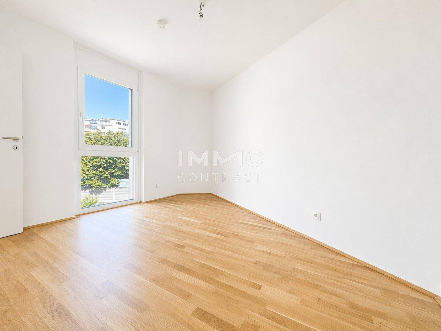 Helles Schlafzimmer mit Parkettboden und einem großen Fenster mit Blick ins Grüne.