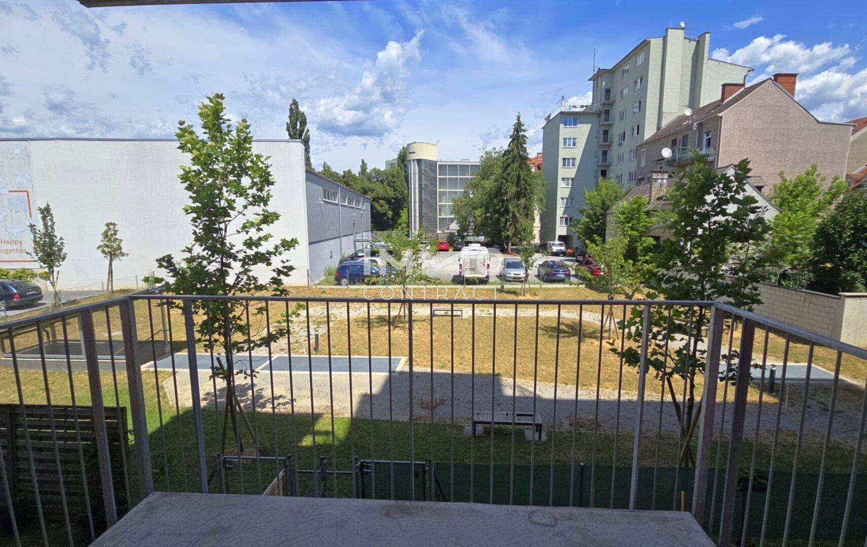 Blick von einem Balkon auf einen begrünten Innenhof mit Spielbereich und umliegenden Gebäuden.