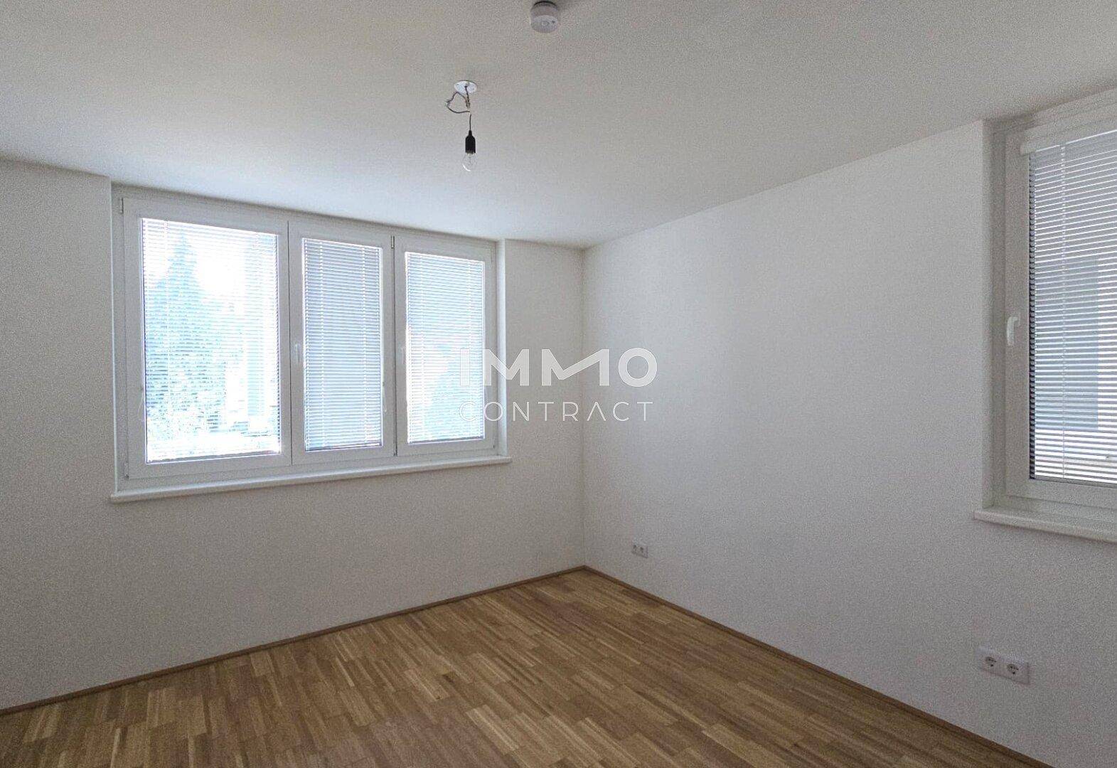 Geräumiges Zimmer mit Parkettboden und mehreren Fenstern, die für eine gute Belichtung sorgen.