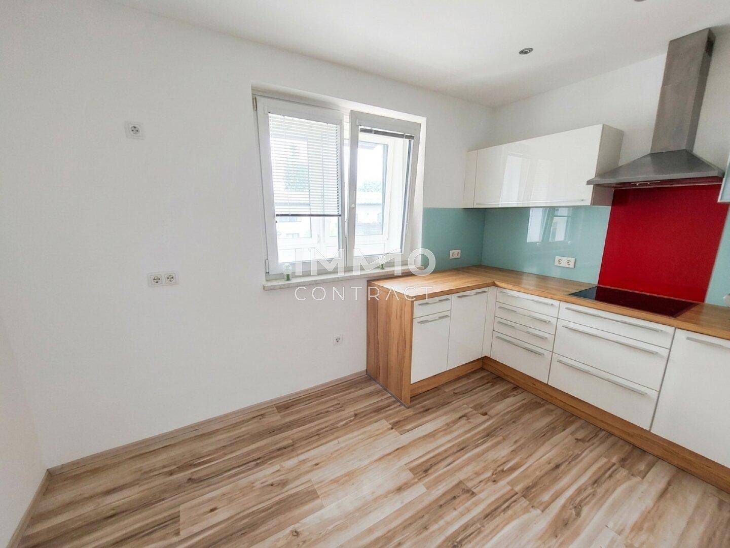 Geräumige Küche mit Laminatboden, weißen Schränken und viel Tageslicht durch das Fenster.