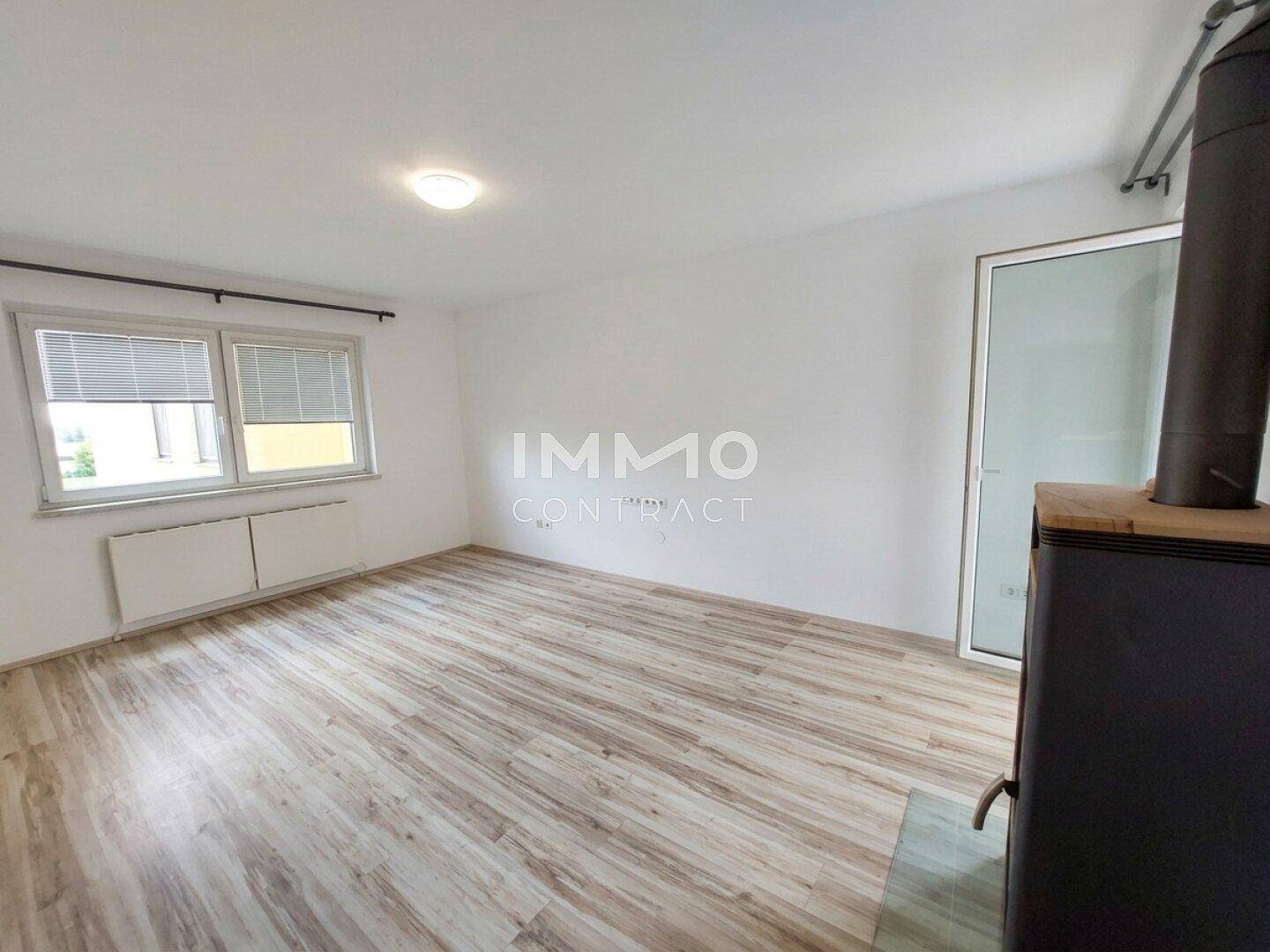 Helles Wohnzimmer mit Laminatboden, Holzofen und Zugang zum Außenbereich.