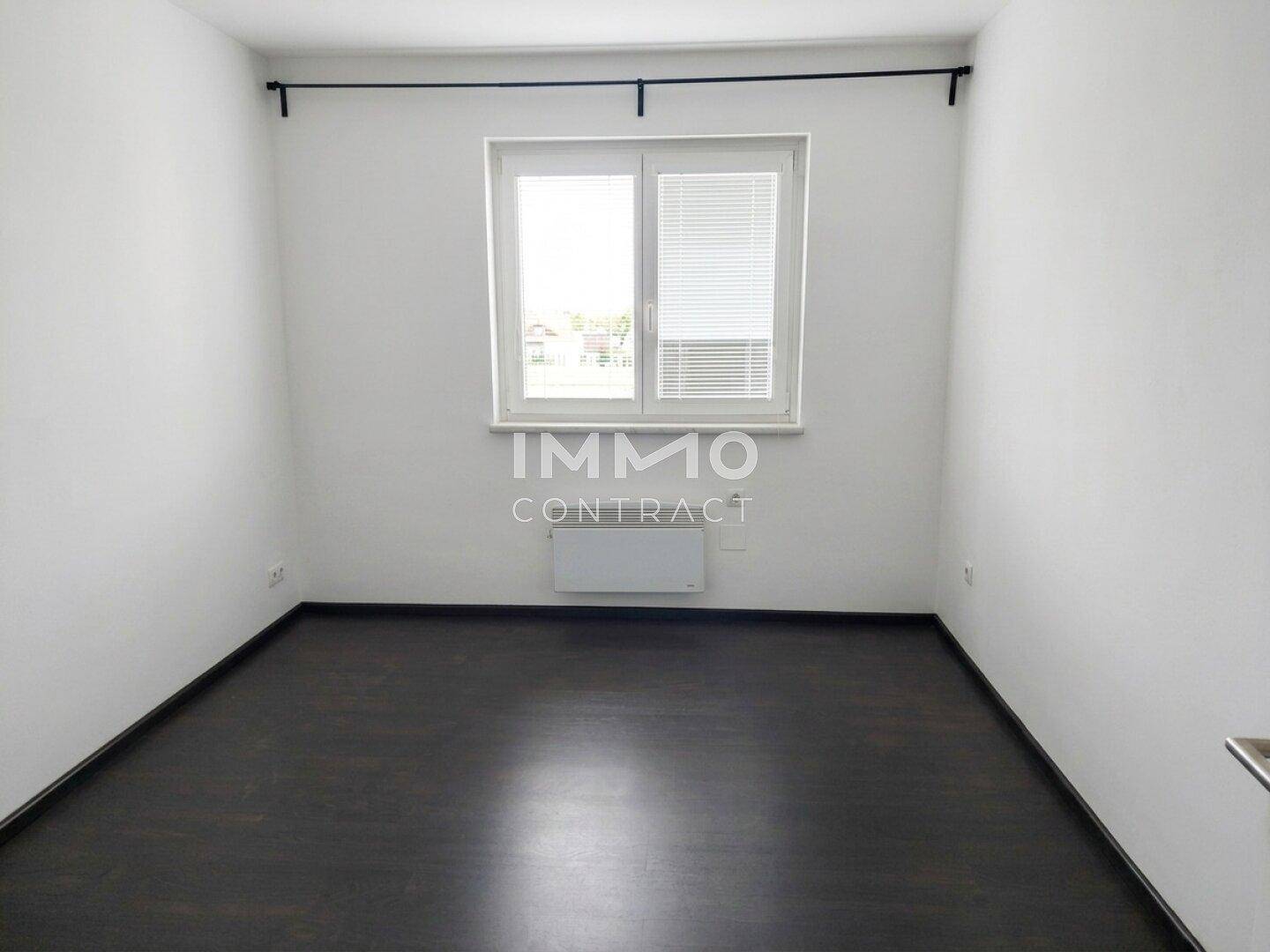 Schlafzimmer mit dunklem Laminatboden und großem Fenster für viel Tageslicht.