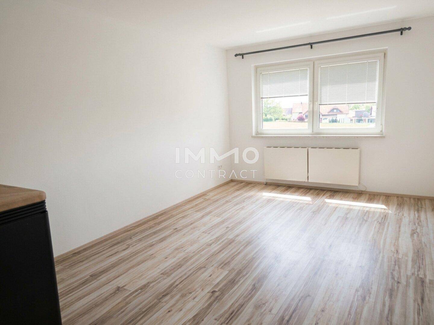 Lichtdurchflutetes Wohnzimmer mit Laminatboden und Blick ins Grüne.