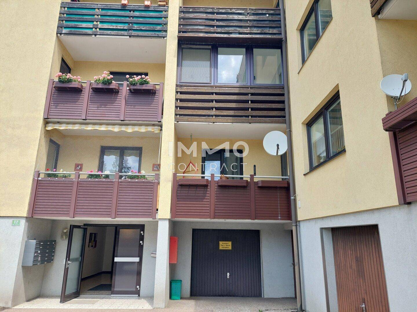 Mehrfamilienhaus mit Balkonen, Garagenzugang und gepflegter Fassade.