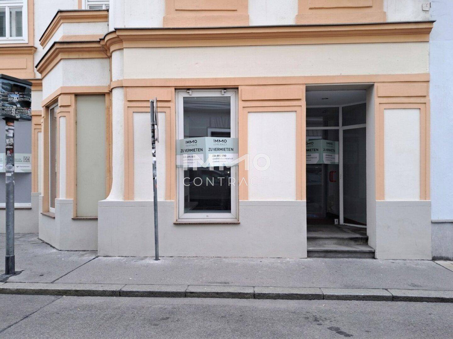 Straßenansicht eines Geschäftsgebäudes mit Eingang und Schaufenstern im Erdgeschoss.
