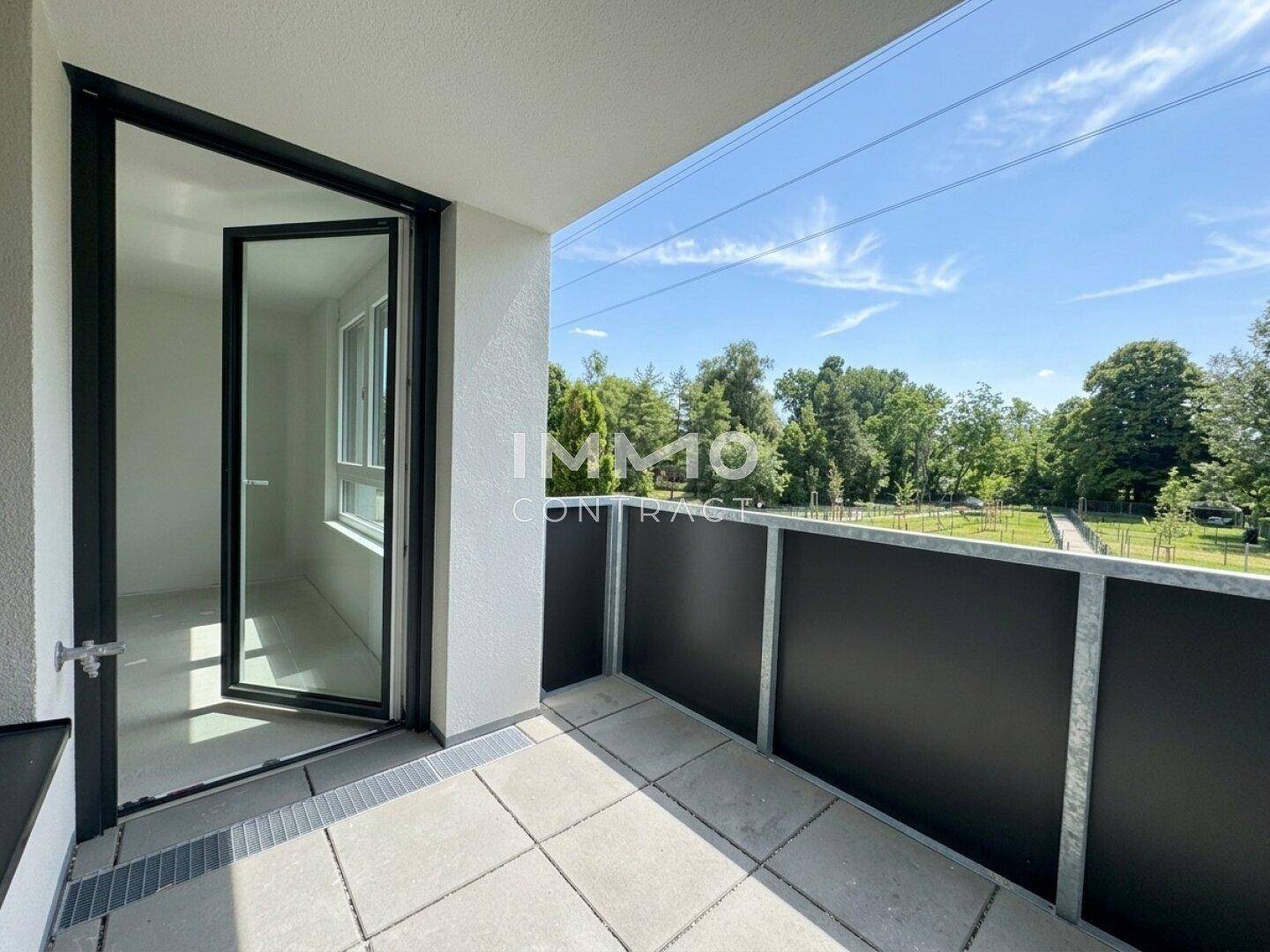 Heller Balkon mit Fliesenboden und weitem Blick auf Bäume und den blauen Himmel.