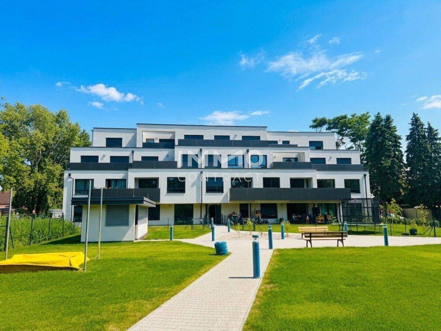 Moderne Wohnanlage mit Spielplatz und weitläufigen Grünflächen unter strahlend blauem Himmel.