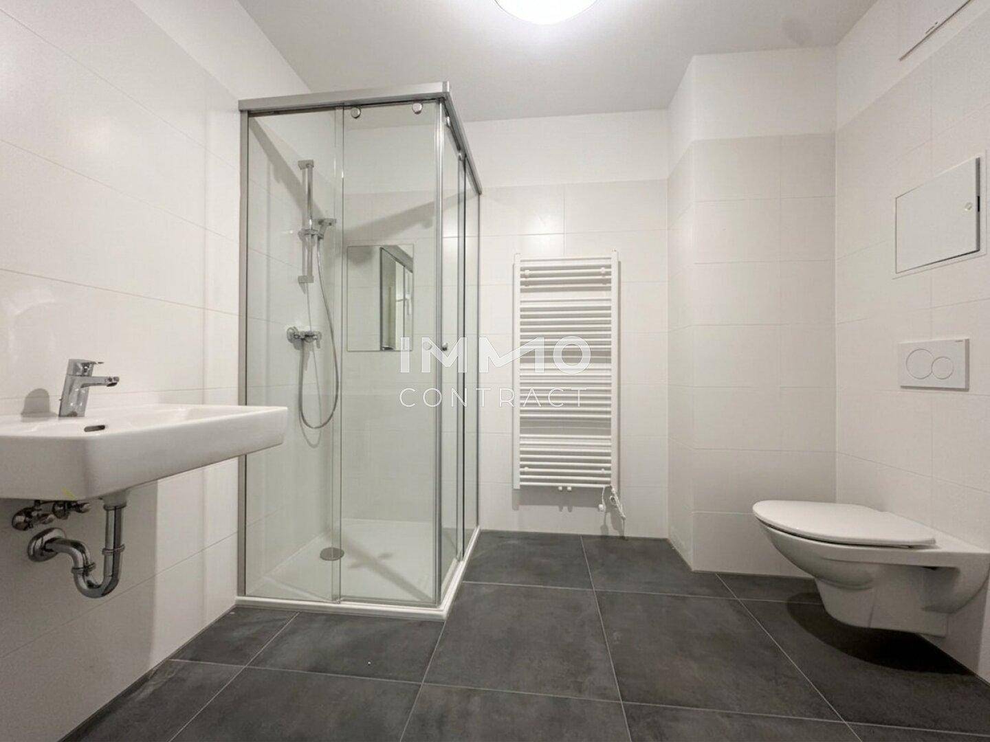 Modernes Badezimmer mit Duschkabine, Wand-WC und beheiztem Handtuchhalter auf Fliesenboden.