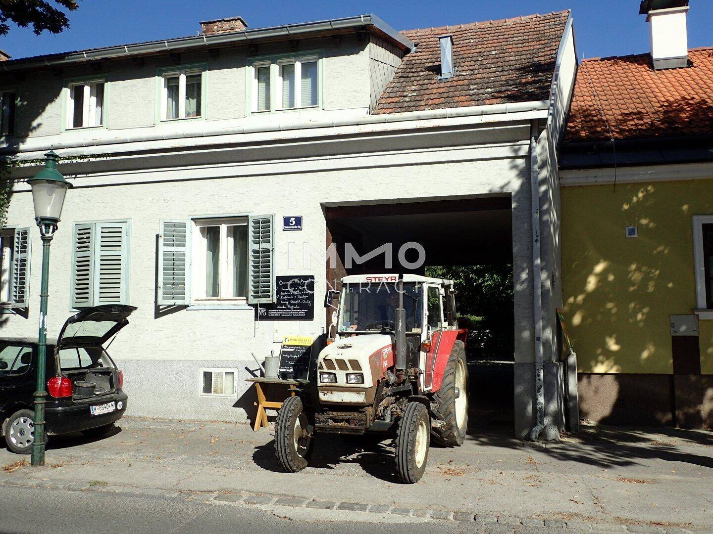 Fassade eines Gebäudes von der Straße aus gesehen, mit einem Traktor unter einem Torbogen.