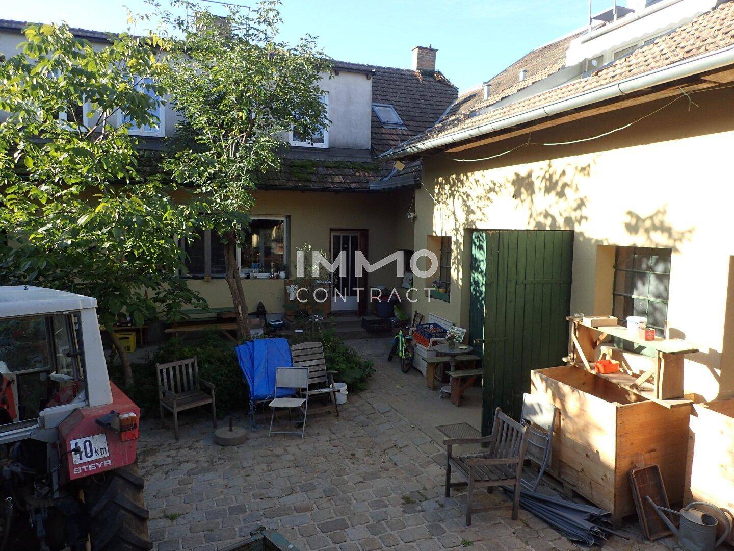 Innenhof mit Pflastersteinen und verschiedenen Gegenständen, umgeben von Gebäuden und Grün.