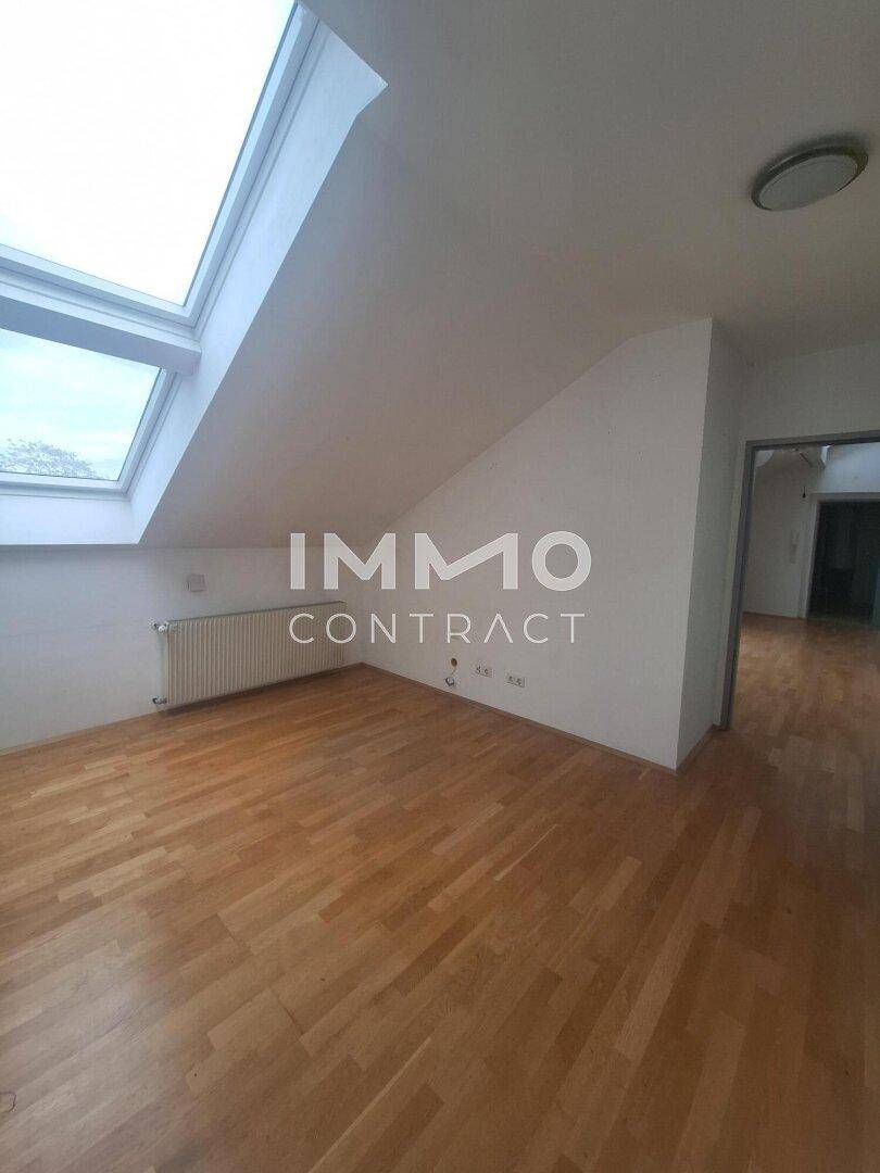 Heller Raum im Dachgeschoss mit schrägen Wänden, Holzfußboden und großem Dachfenster.