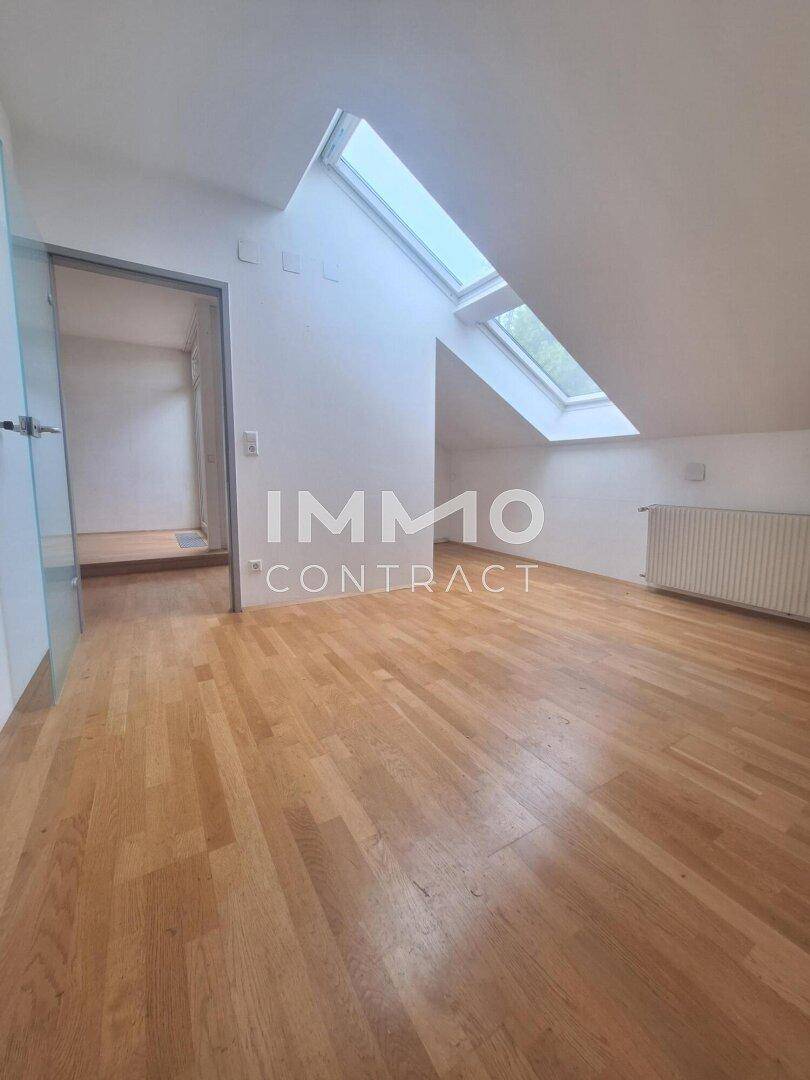 Geräumiger Dachgeschossraum mit Holzfußboden, schrägen Wänden und viel Tageslicht durch Dachfenster.