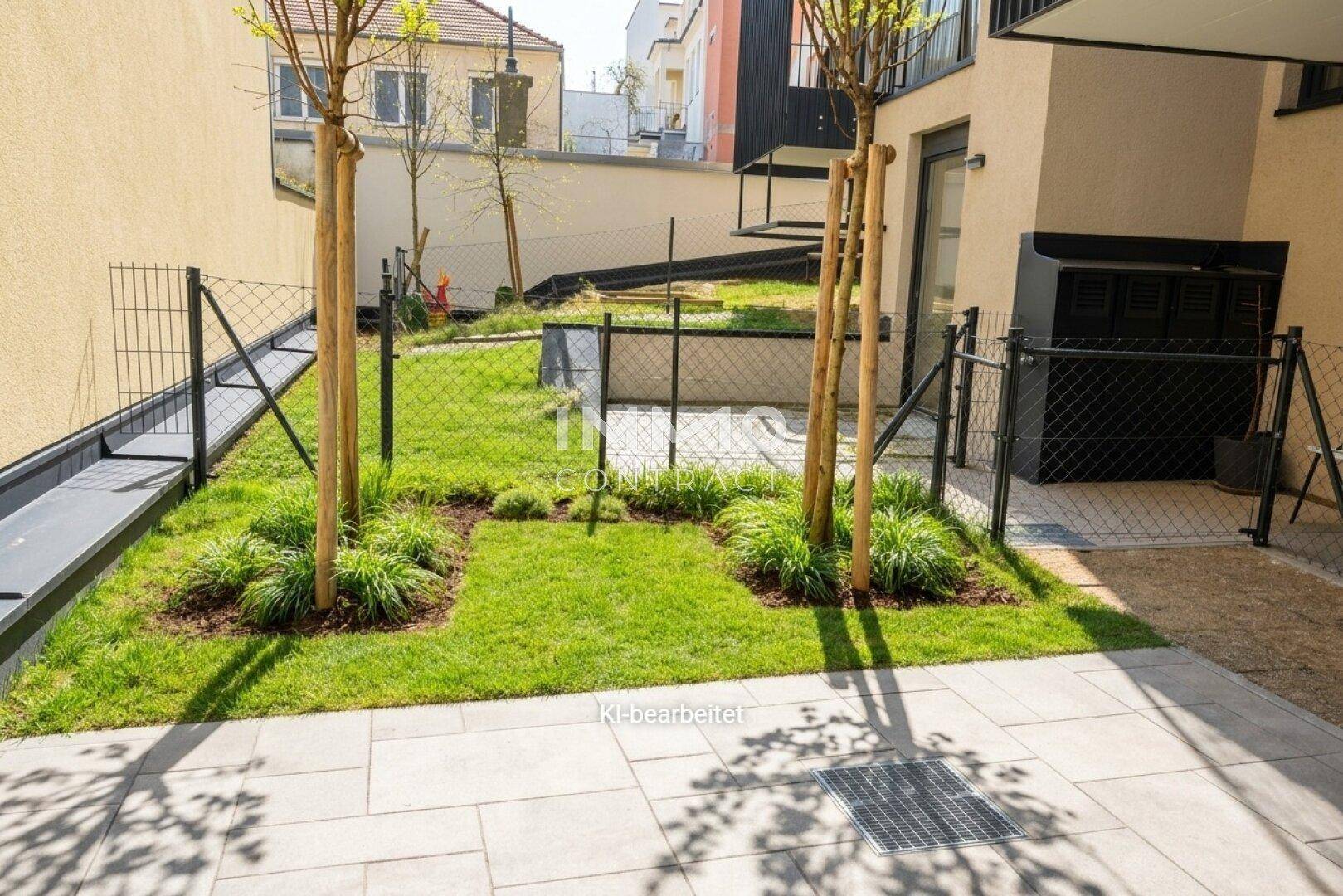 Kleiner, neu angelegter Gartenbereich mit Rasenfläche, jungen Bäumen und gepflastertem Weg.