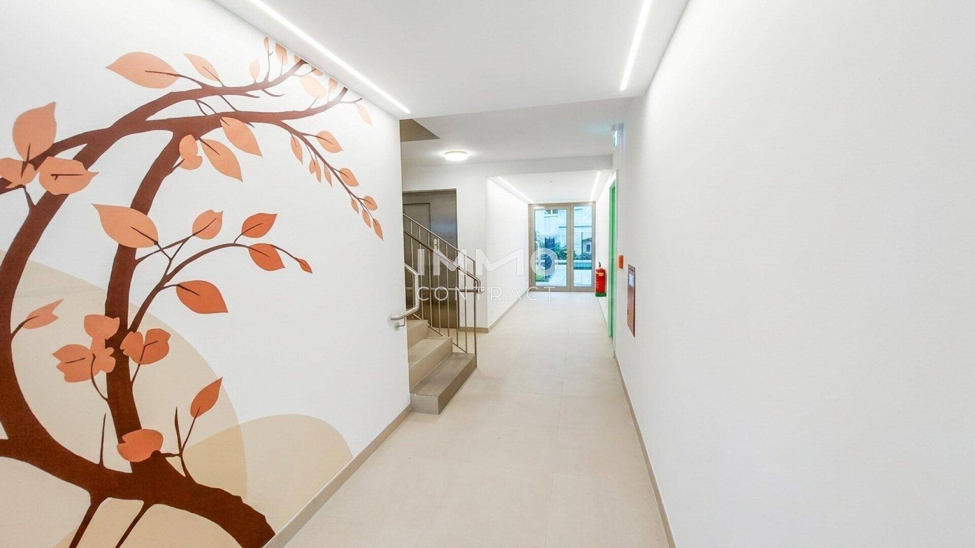Heller Flur mit dekorativer Wandmalerei und Zugang zu einem Treppenhaus.
