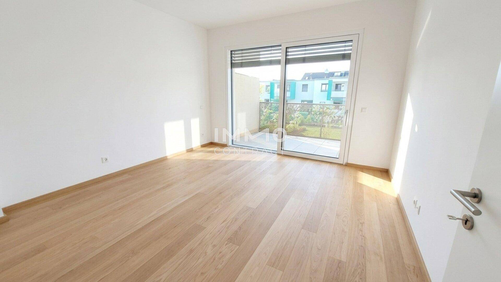 Heller, leerer Raum mit Holzboden und Zugang zu einem kleinen Außenbereich.