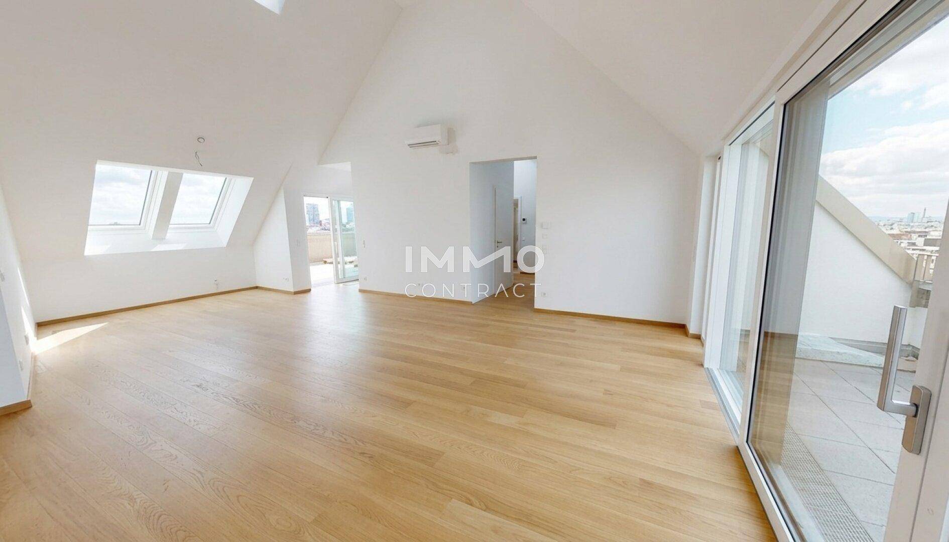 Geräumiger Dachgeschossraum mit Holzboden, schrägen Decken und Zugang zu einer Terrasse.