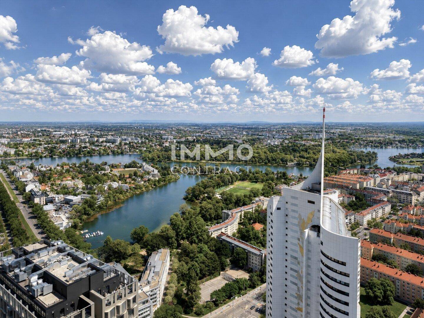 Panoramablick auf die Stadt mit dem Donauturm, dem See und der umliegenden grünen Landschaft.