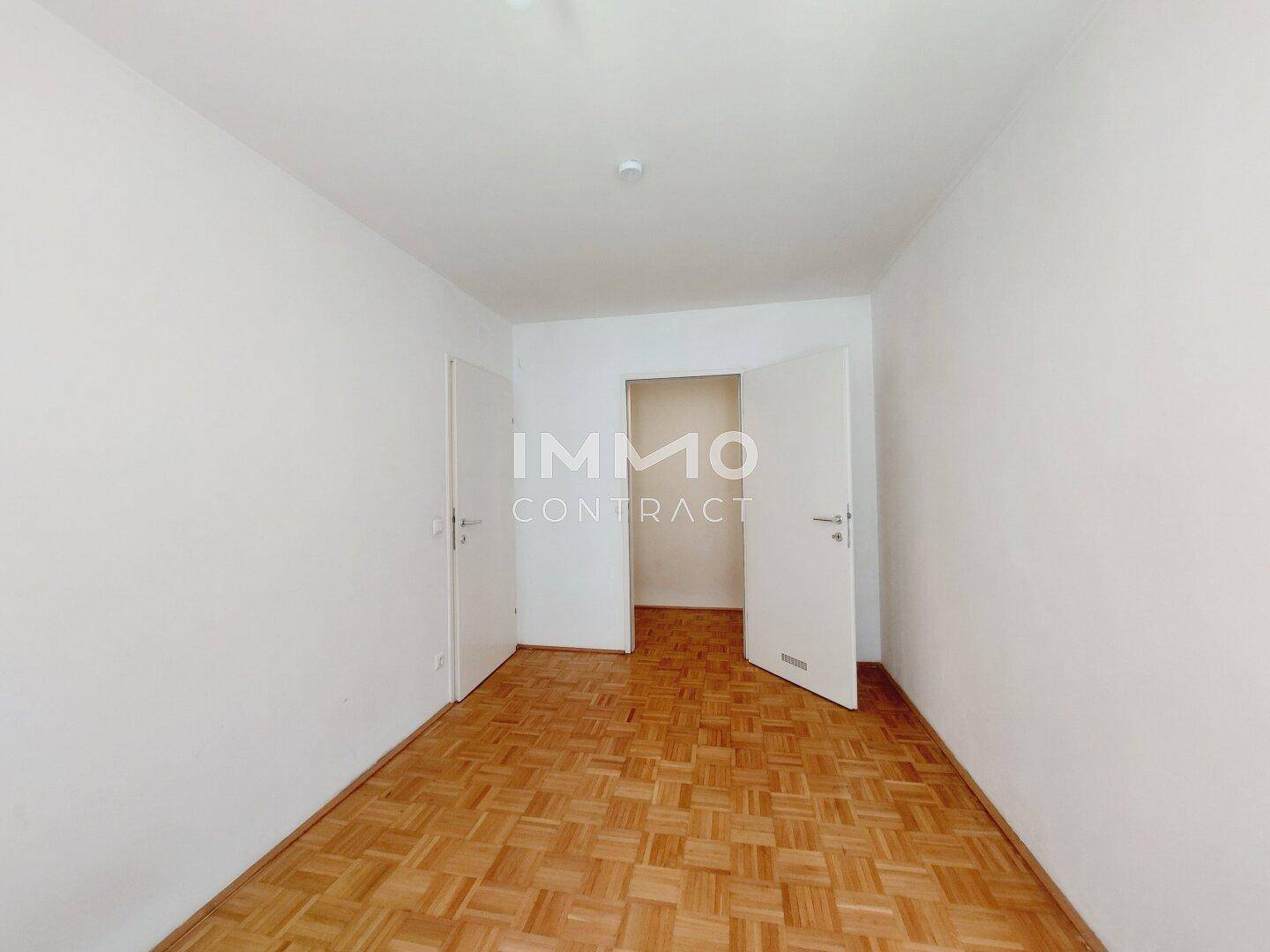 Leeres Zimmer mit Parkettboden und zwei weißen Türen, bereit zur individuellen Gestaltung.