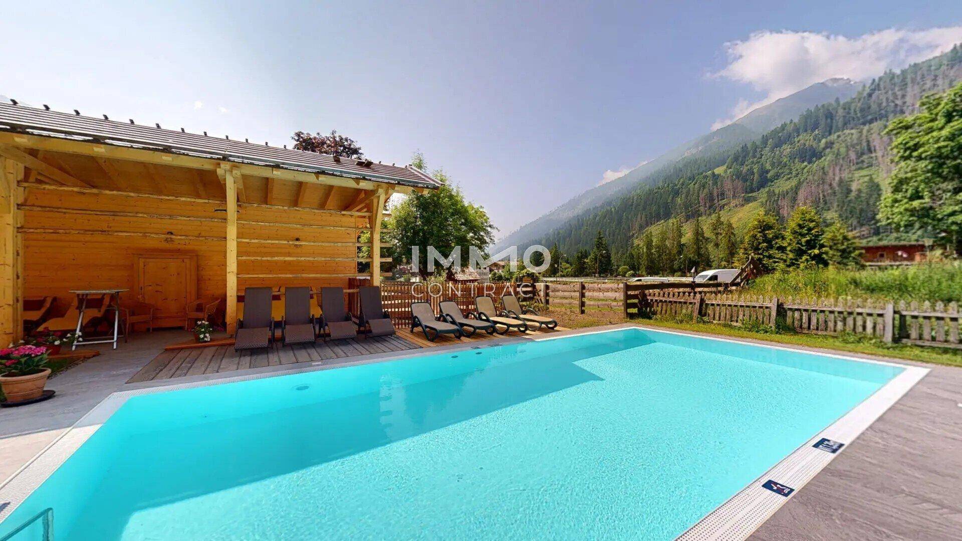 Außenpoolbereich mit Liegestühlen und einer Holzhütte, umgeben von einer beeindruckenden Berglandschaft.