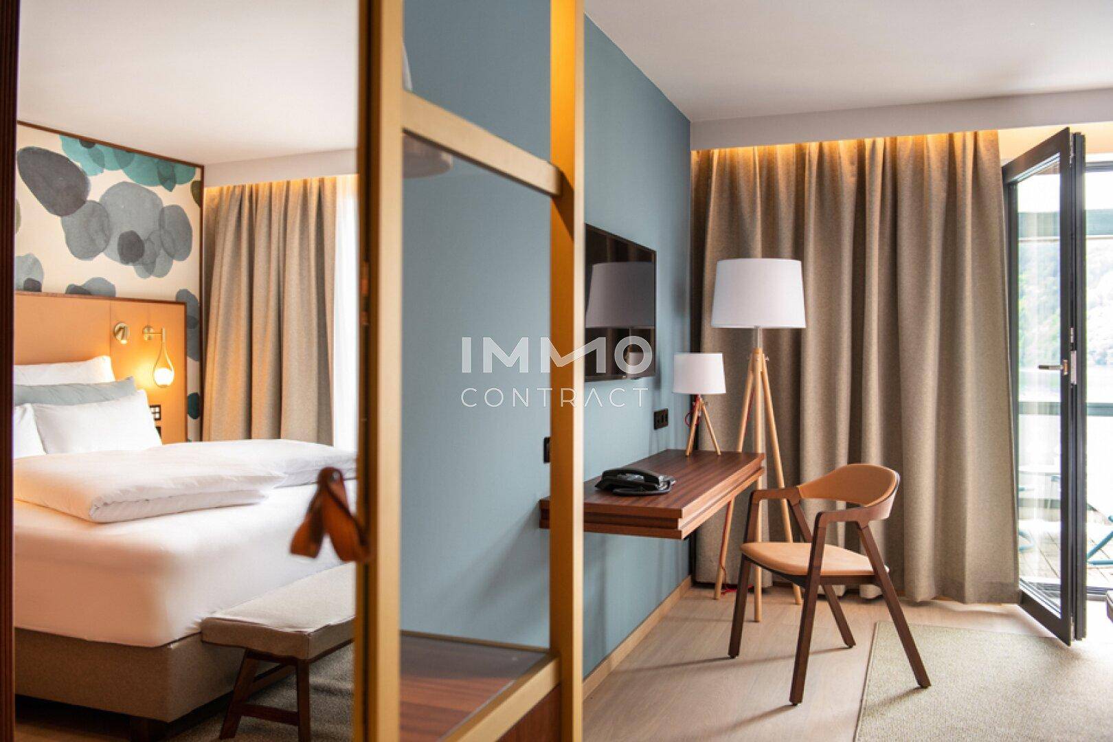 Gemütliches Schlafzimmer mit Schreibtisch, großem Bett und Zugang zu einem Balkon mit Seeblick.