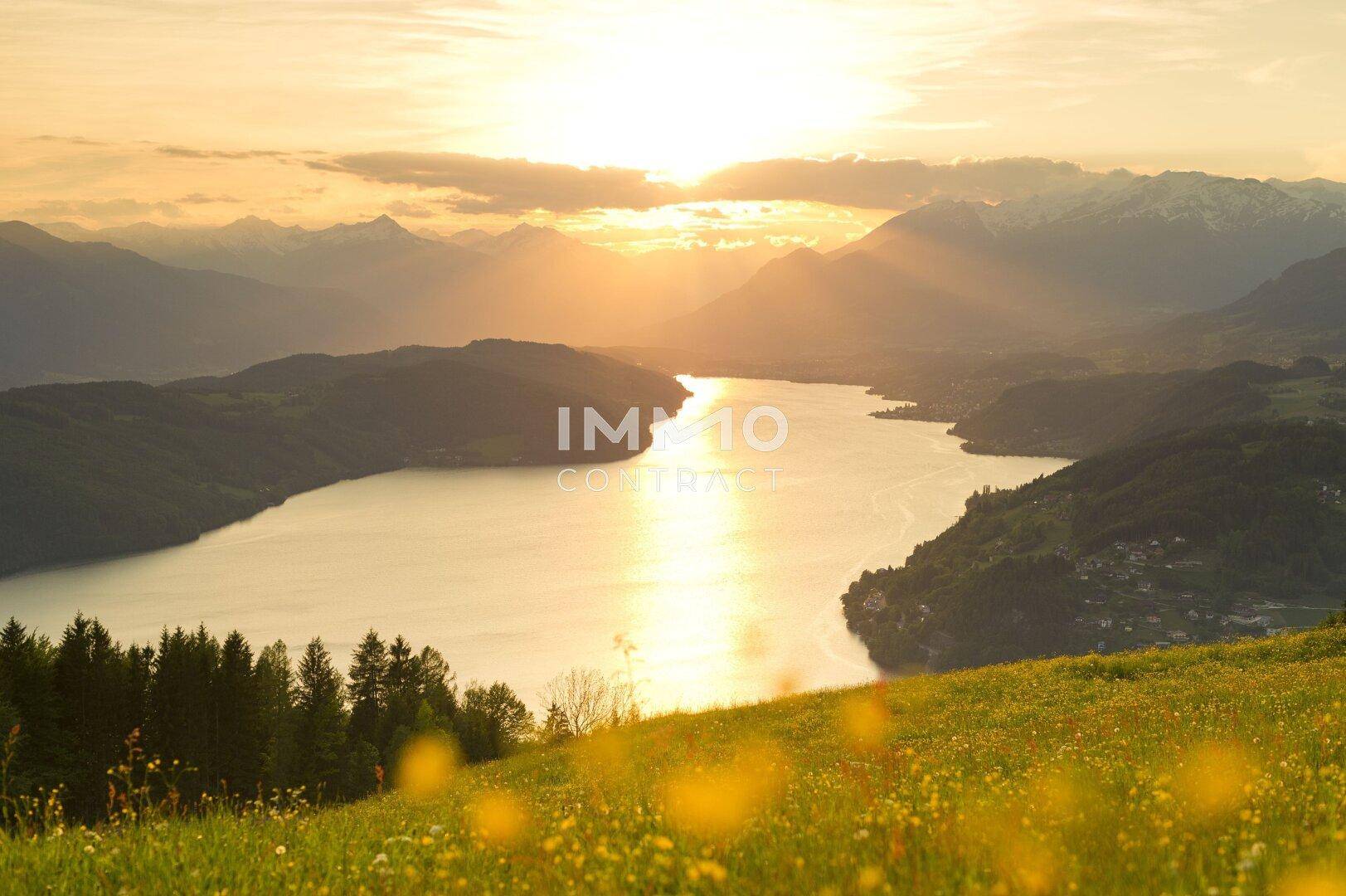 Atemberaubender Sonnenuntergang über einem See und den umliegenden Bergen, umgeben von grünen Wiesen.