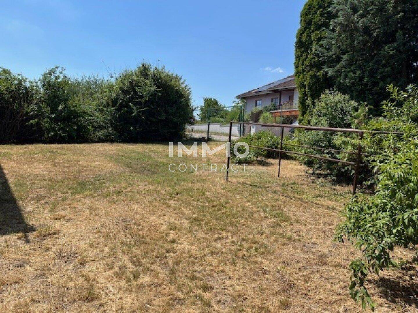 Große Rasenfläche im Garten mit Zaun und Blick auf ein Nachbarhaus in der Ferne.