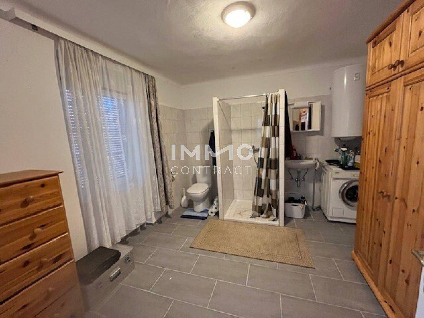 Badezimmer mit Dusche, WC, Waschmaschine und Holzschränken, funktional eingerichtet.
